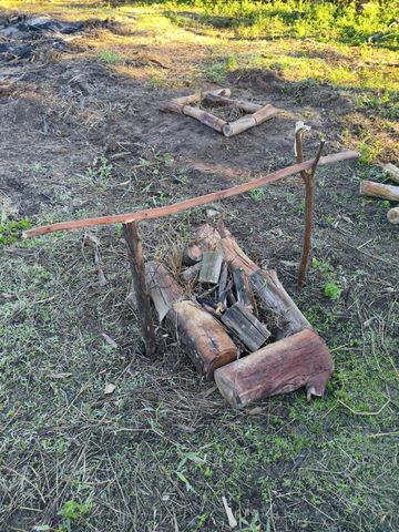 Troncos e gravetos organizados no solo, com suporte de madeira, durante uma instrução de fogueiras.