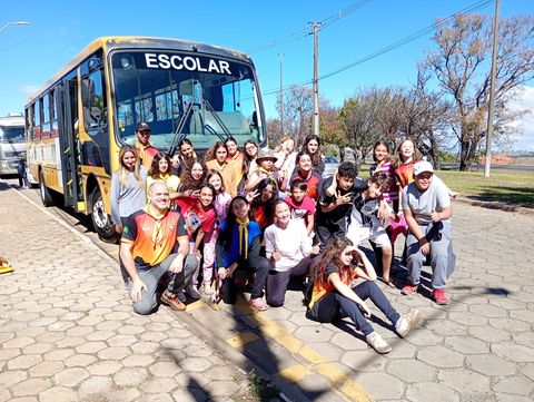 Grupo reunido em frente a um ônibus escolar, em registro do acampamento de instruções.